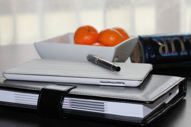 Ein Notizbuch auf dem Smartphone und Stift liegen, Schale mit Obst im Hintergrund, Schreibtisch